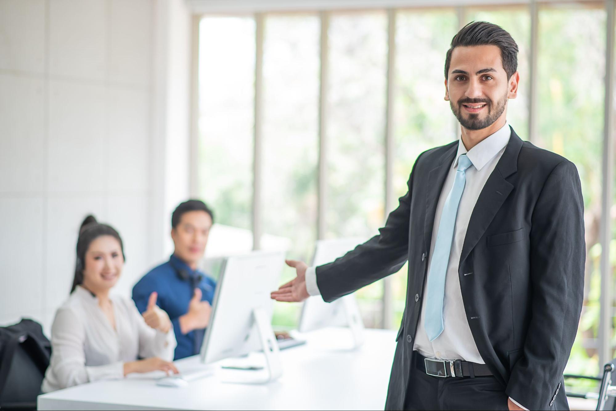 A boss in a business coat stands posing, welcoming a visitor.