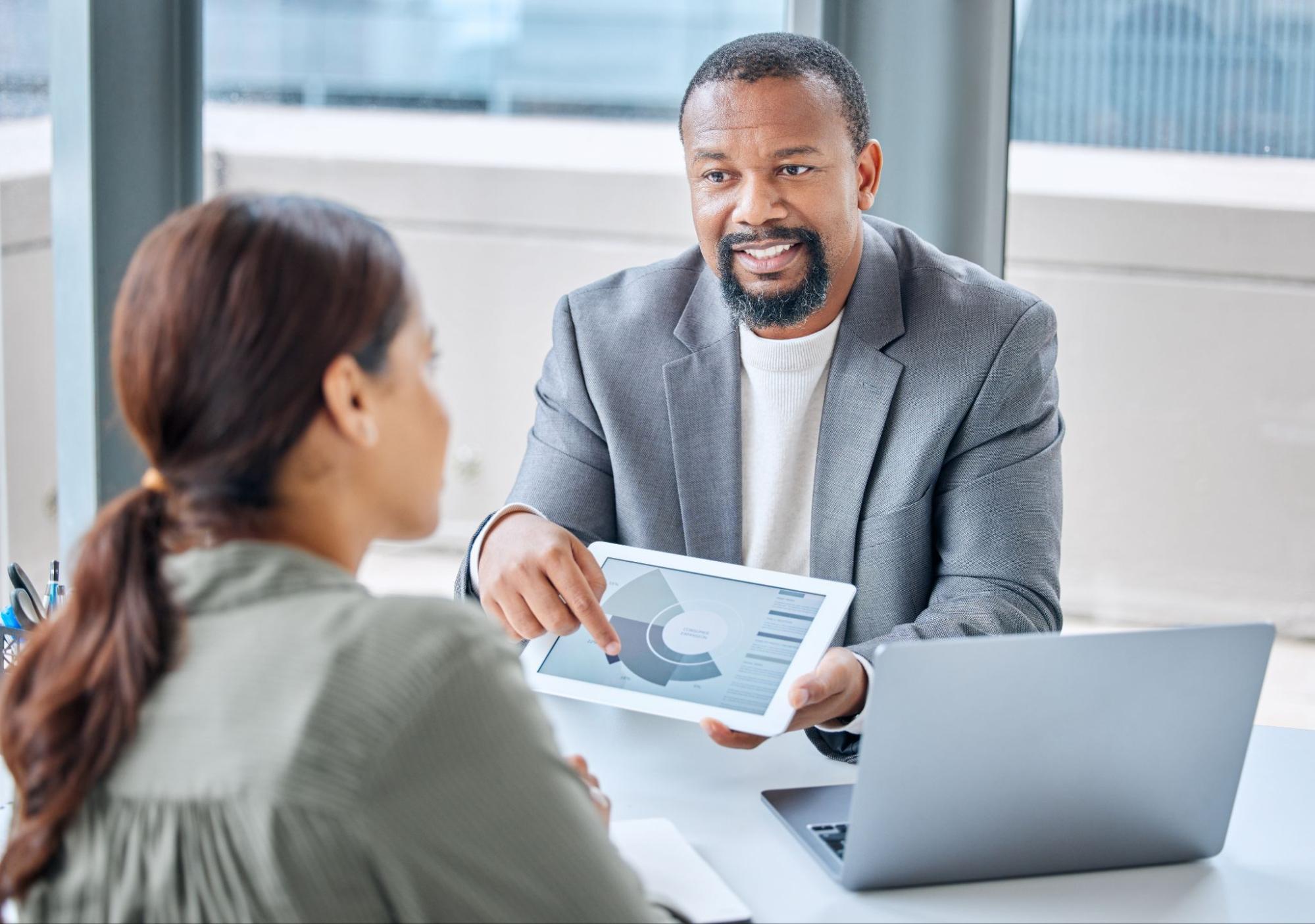 A male employee is discussing a presentation to a woman using a tablet.