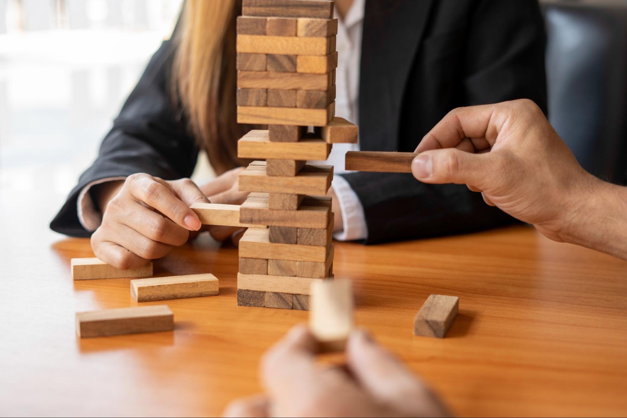 Two business people play a game of Jenga, symbolizing risk management.