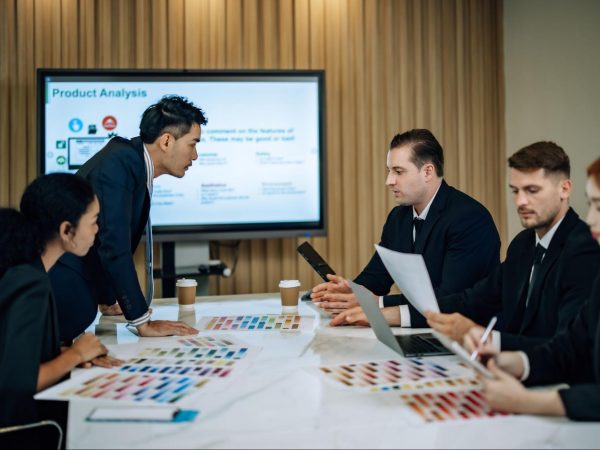 A diverse team engages in design thinking, gathering insights, and proposing solutions while a big screen on the wall displays key information.