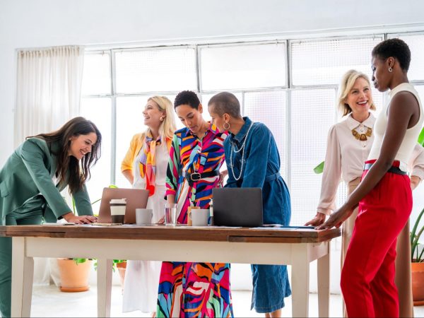 A diverse group of businesswomen in vibrant attire discussing a product launch strategy in a modern office setting.