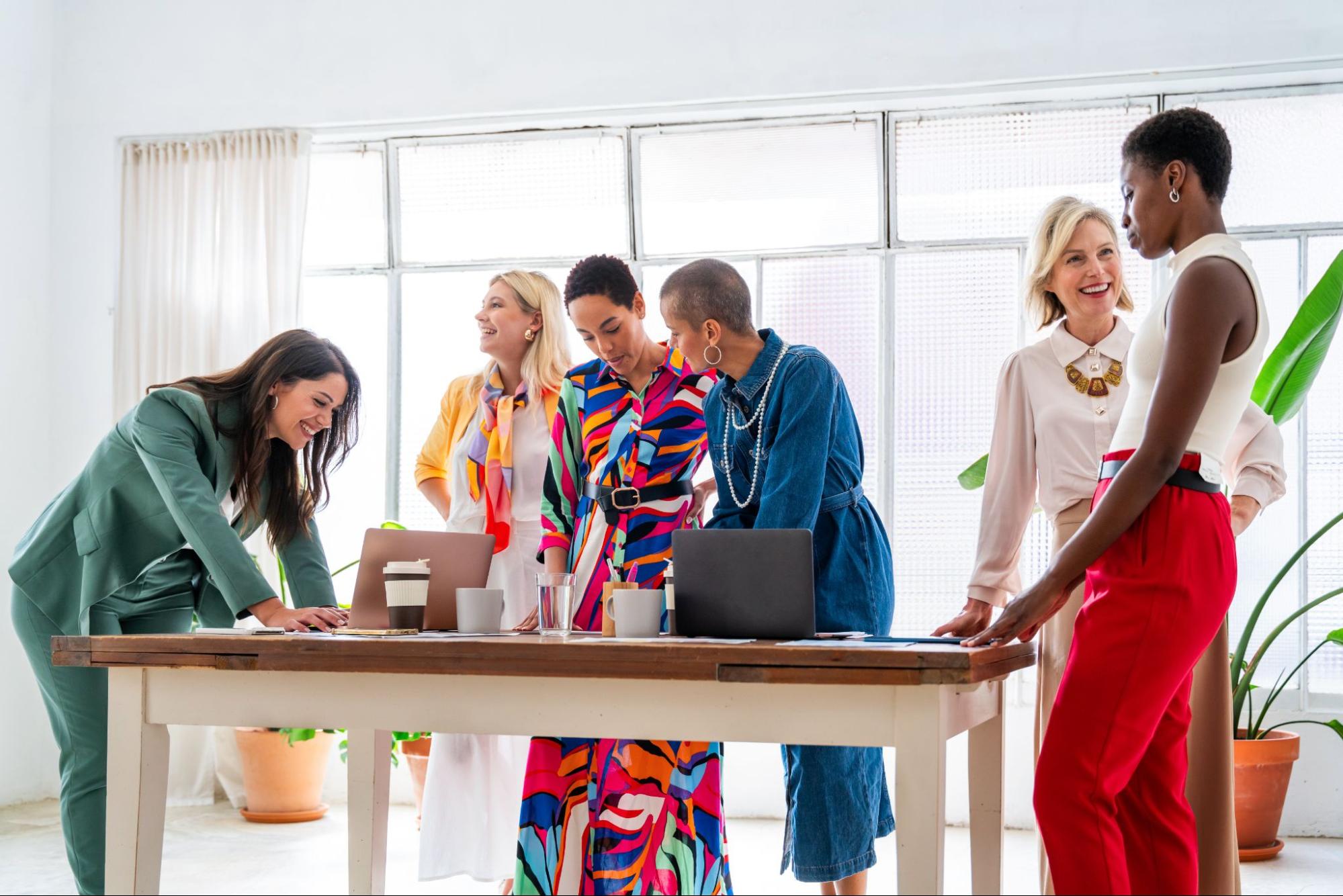 A diverse group of businesswomen in vibrant attire discussing a product launch strategy in a modern office setting.