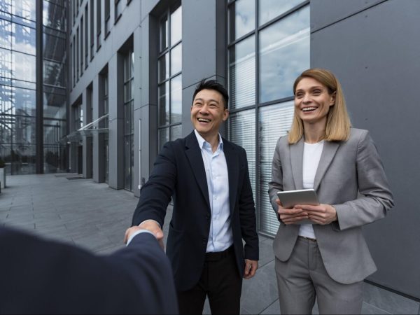 A male manager shaking hands with a leader while a female manager greets with a smile