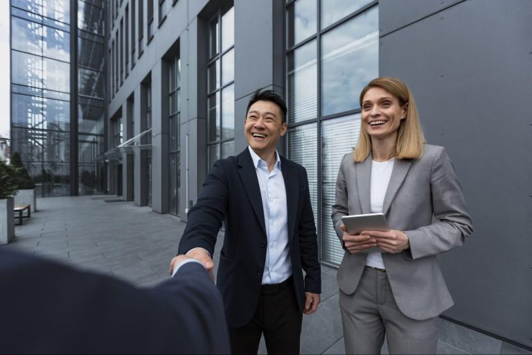 A male manager shaking hands with a leader while a female manager greets with a smile