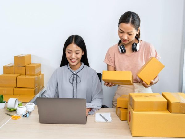 A woman using a laptop and the other holding packages.