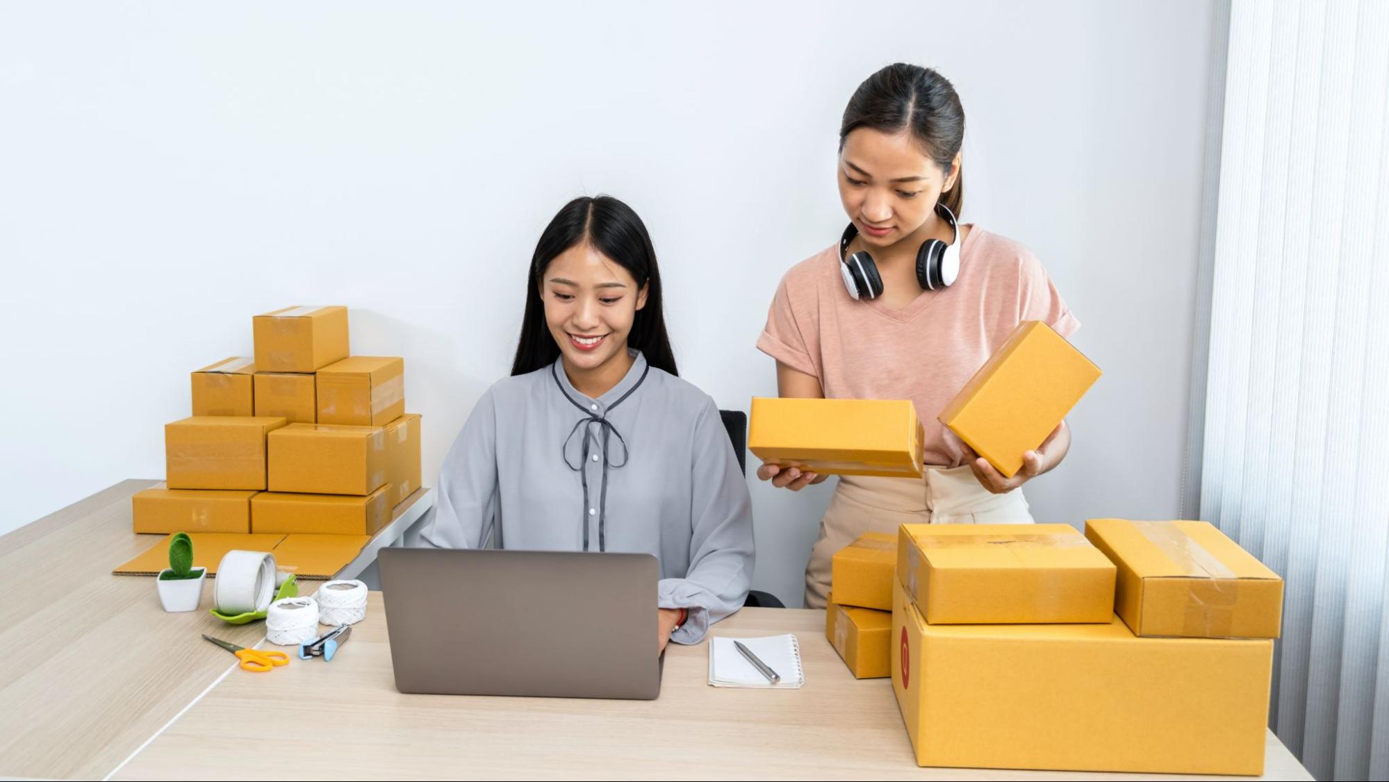 A woman using a laptop and the other holding packages.