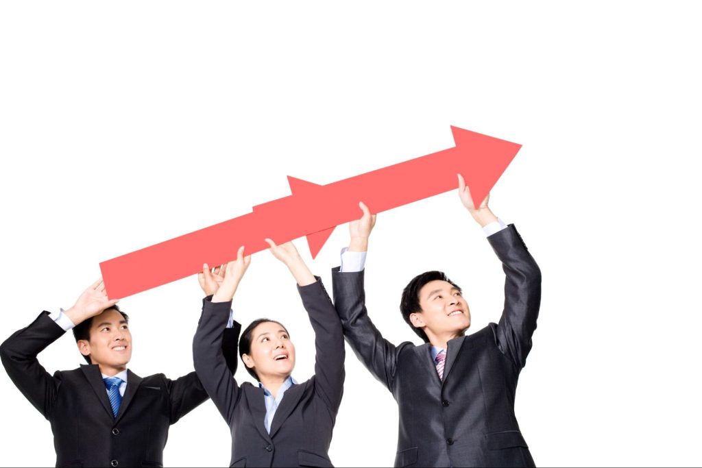 Three business partners in black suits hold up a large red arrow sign above their heads. 